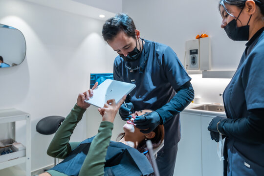 Dentist showing teeth whitening results on tablet to patient in modern clinic