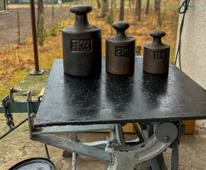 Old cast iron weights standing on a pine board, in the background a village and a sparse forest