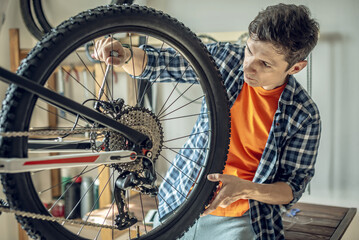 A male bicycle mechanic in the repair shop disassembles a mountain bike and repairs it. Maintenance...