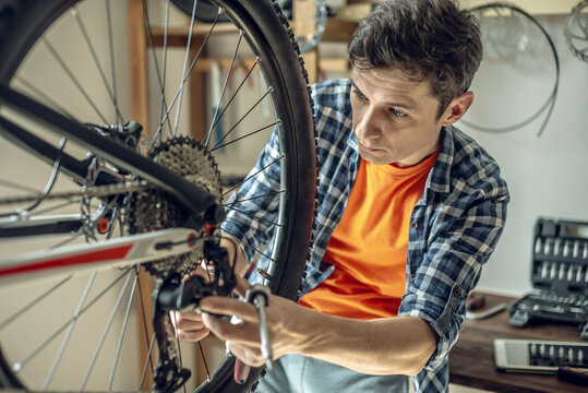 A male bicycle mechanic in the repair shop disassembles a mountain bike and repairs it. Maintenance concept, preparation for the new season