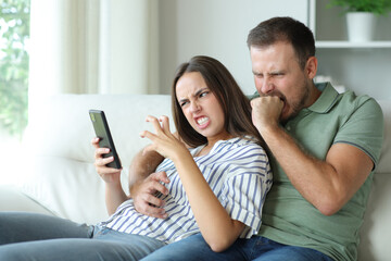 Angry couple at home checking mobile phone content