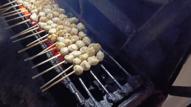 Delicious meatball skewers grilling over hot charcoal on a street food stall.