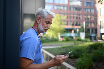 Healthcare worker outside hospital and checking phone during break.