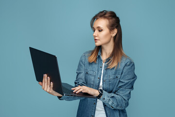 Serious young woman in jeans shirt using computer or laptop over blue background