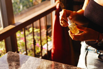 Female hands holding a glass bottle with natural oil for body and hair against the background of...