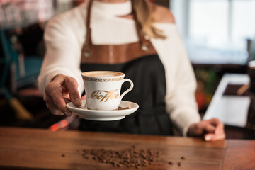 Young blonde barista hands over fresh coffee to customer at café counter in Germany