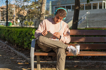 Young man listening to music and using tablet in a park