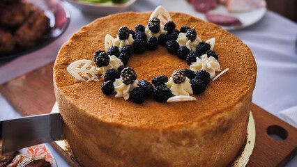 Cutting delicious sponge cake decorated with blackberries and white chocolate on festive table