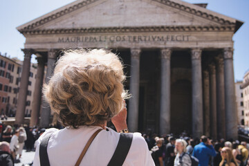 Senior tourist capturing stunning photos of the pantheon in rome, italy, surrounded by a lively crowd of visitors enjoying the iconic landmark on a bright, sunny day