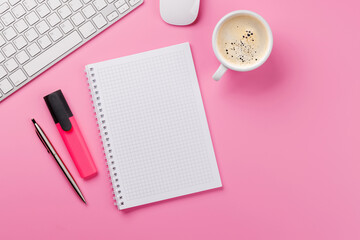 Top view of a pink desk with office supplies, coffee cup, and blank notepad