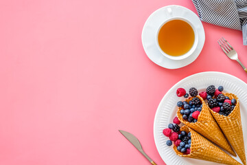 Fresh berries in waffle cones with tea and tableware on pink kit