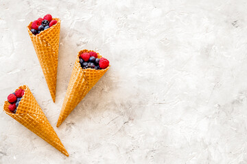 Summer breakfast with fresh berries in waffle cones on light sto