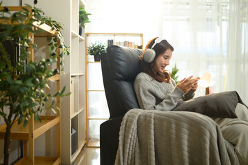 Obraz premium Young asian woman enjoys playing a mobile game sitting on armchair at home