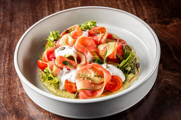 A fresh, vibrant salad featuring sliced tomatoes, greens, and creamy dressing. Perfect for healthy eating, this dish showcases colorful vegetables on a rustic wooden table.