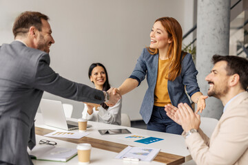 Female team leader shaking hands with businessman at boardroom in front of team of data experts.