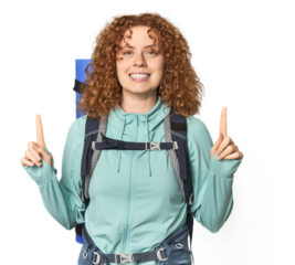 Young Caucasian redhead ready for hiking indicates with both fore fingers up showing a blank space.