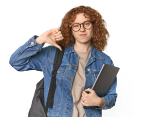 Young Caucasian redhead student with books showing a dislike gesture, thumbs down. Disagreement concept.