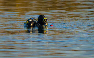 Heavily equipped diver on lake, reflections on blue water surface