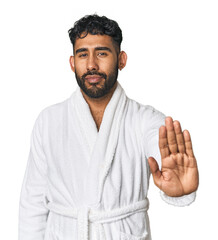 Hispanic male in a robe in studio standing with outstretched hand showing stop sign, preventing you.