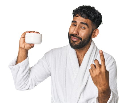 Hispanic male with moisturizer in studio pointing with finger at you as if inviting come closer.