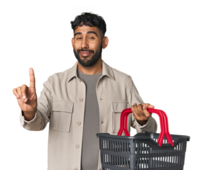 Hispanic male holding shopping basket in studio showing number one with finger.