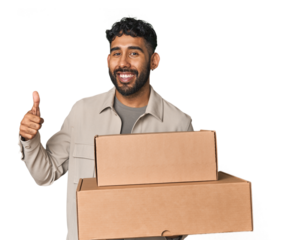 Hispanic male holding cardboard boxes in studio smiling and raising thumb up
