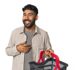 Hispanic male holding shopping basket in studio looks aside smiling, cheerful and pleasant.
