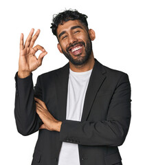 Hispanic businessman in suit in studio winks an eye and holds an okay gesture with hand.