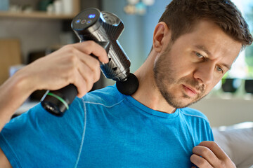 Fototapeta premium Man applies massage gun to relieve tension in neck and shoulder area. Male athlete doing self-massage therapy with percussion device for recovery after training