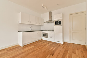 A sleek and modern kitchen featuring white cabinetry, a black countertop, and wooden flooring, creating a bright, functional space for cooking and entertaining.