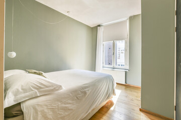 A serene bedroom with soft natural light filtering through a window, showcasing minimalistic design and warm wooden floors.