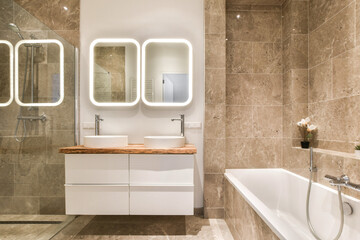 A sleek modern bathroom featuring dual sinks, a stylish bathtub, and elegant lighting. The neutral...