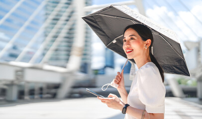 Business asian woman holding UV protection umbrella with shopping bags using smartphone on sunny day © dodotone