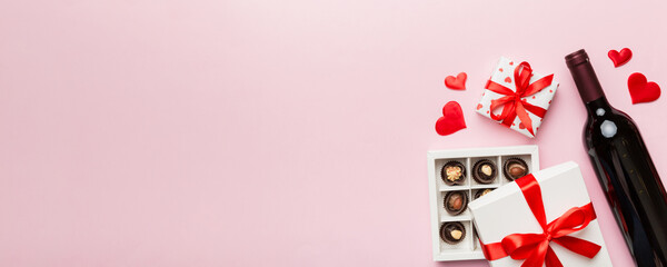 Bottle of red wine on colored background for Valentine Day with gift and chocolate. Heart shaped with gift box of chocolates top view with copy space