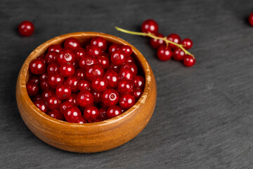 ripe red currant berries poured in a wooden bowl, harvest small red currant berries on the kitchen table in a bowl