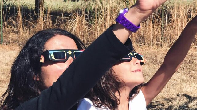 Caucasian woman holding her young daughter excitedly watching the total solar eclipse with special glasses