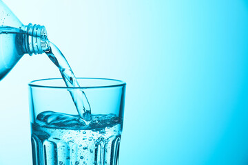 Pouring soda water from bottle into glass on light blue background, closeup. Space for text