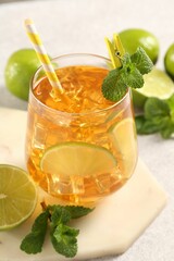 Refreshing iced tea with slices of lime, mint and drinking straw in glass on light table, closeup