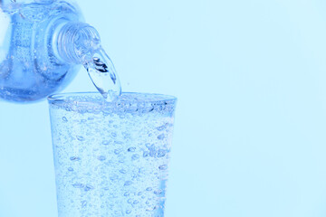 Pouring soda water from bottle into glass on light blue background, closeup. Space for text