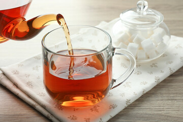 Pouring freshly brewed tea from teapot into cup at wooden table, closeup