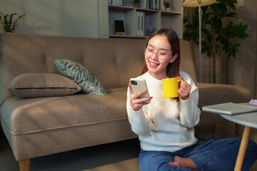 Smiling young woman sitting comfortably on the floor, enjoying a warm cup of coffee while browsing...