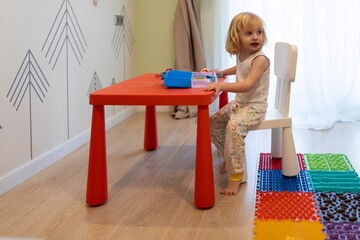 Young child plays at a colorful table in a bright, cheerful playroom filled with toys and soft...