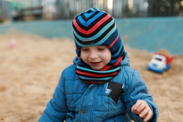 Child enjoying playtime in a sandbox at a park during a cool autumn afternoon while wearing a colorful hat and scarf