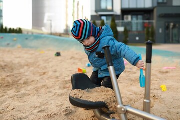 Child playing in sandy playground with shovel and bucket on a clear day