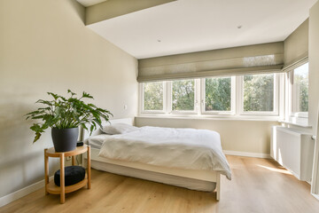 A serene bedroom featuring a cozy bed, a plant, and large windows that provide ample natural light, creating a tranquil atmosphere.