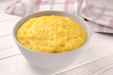 Delicious corn porridge in a bowl on a white wooden table.