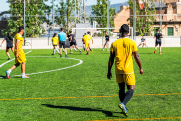 young black african american man playing a match in a football pitch on a sunny day with a mixed race team. Young athlete practicing soccer doing sport and exercise