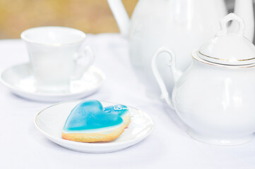 Elegant Tea Set with Blue Heart-Shaped Sugar Cookie on White Surface..