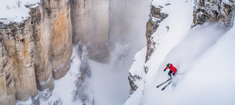 Extreme skier skiing down steep snowy mountain slope between cliffs
