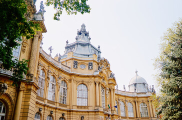 Fototapeta premium A beautiful historic building with ornate architecture, featuring intricate sculptures and a domed roof. Surrounded by lush greenery, the structure showcases large windows and decorative details.